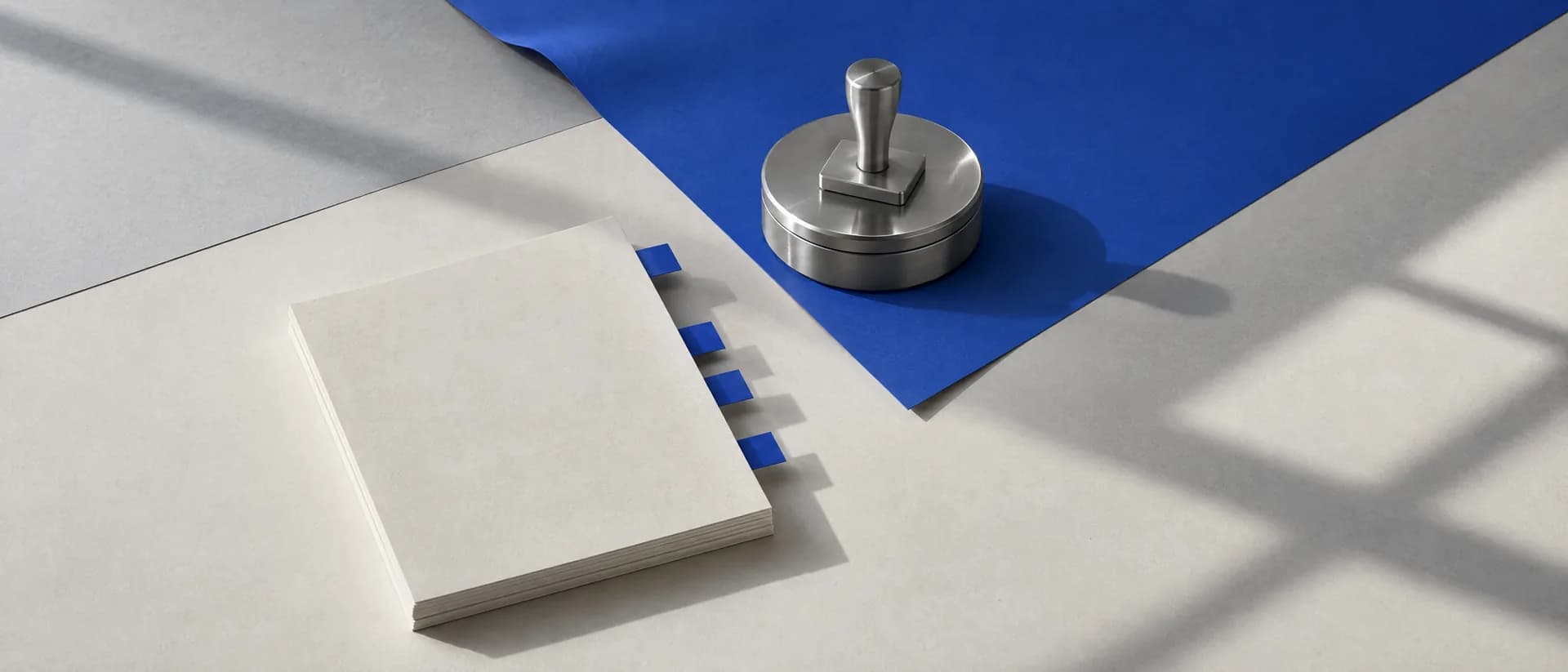 A stack of blank pages flagged with four cobalt tabs beside a dry rubber stamp resting on its closed ink tin.