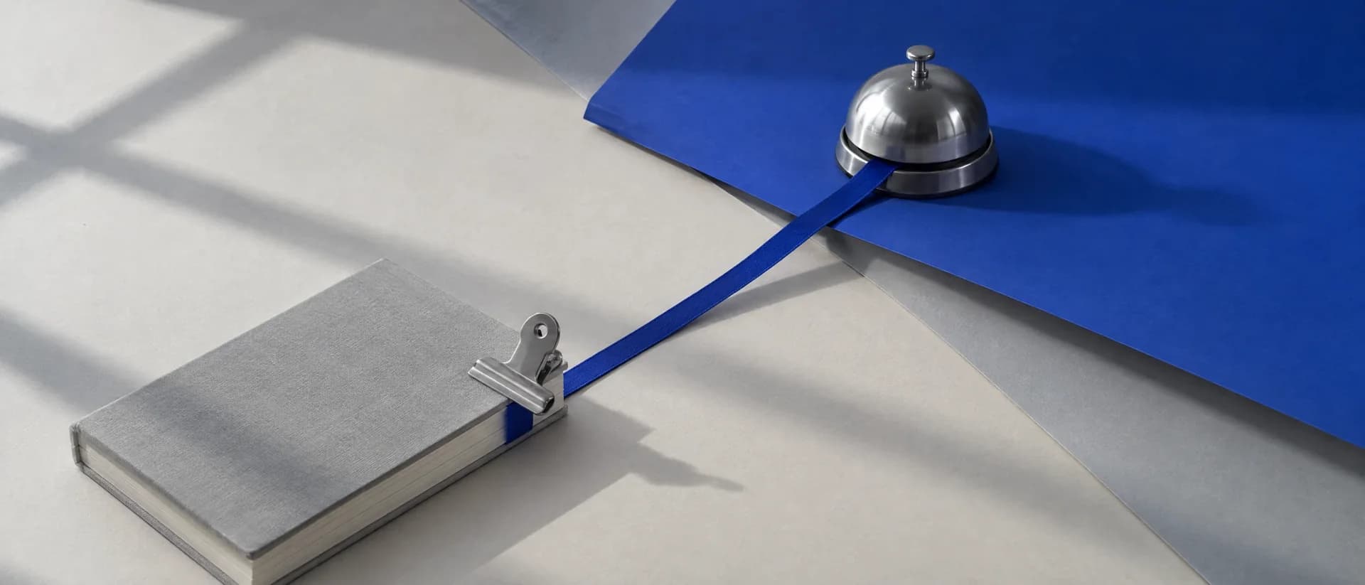 A reception bell on cobalt paper with a ribbon running into a closed diary.