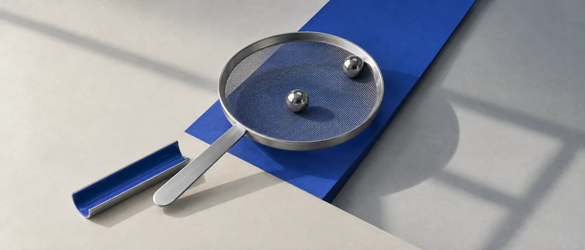 Two steel balls resting on the same fine sieve, neither one through the mesh.