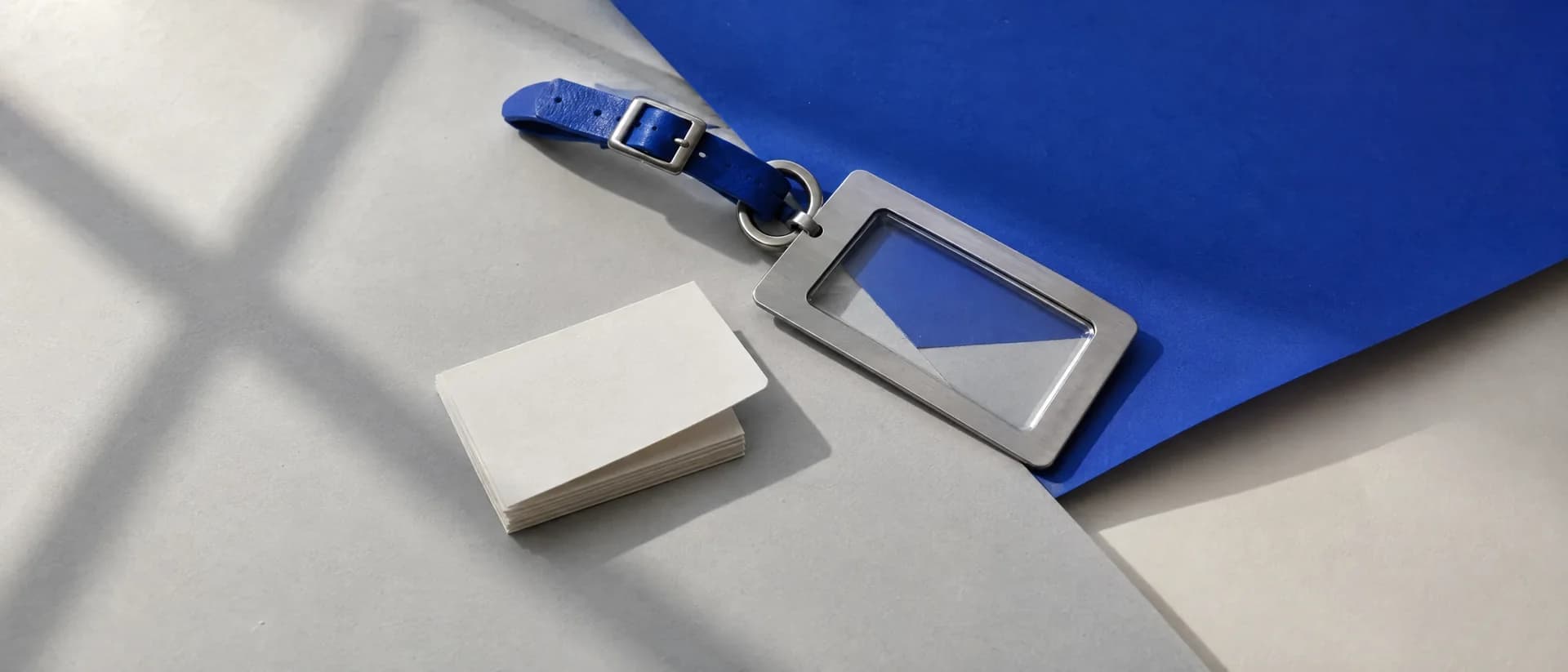 A steel luggage tag with an empty clear window beside a stack of blank cards.