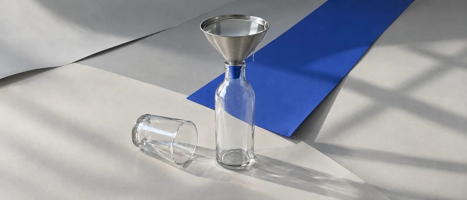 A steel funnel full of water on a dry glass bottle, its spout blocked by a cobalt bung.