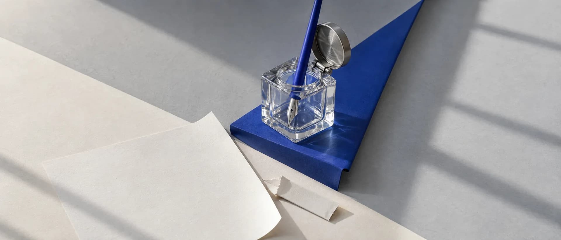 A new steel pen nib standing in an empty glass inkwell beside a blank sheet.