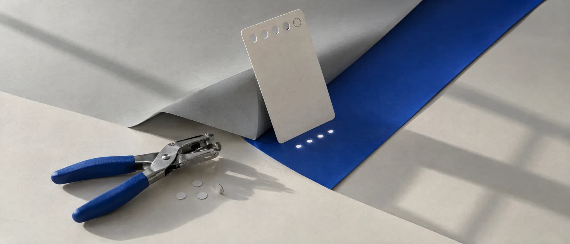 A card ticket with four punched holes and one intact circle; light through the holes casts four dots on cobalt paper.